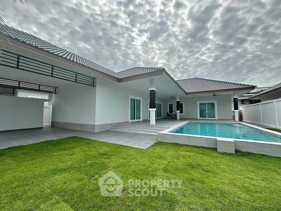 Stunning modern house with private pool and lush green lawn under a dramatic sky.