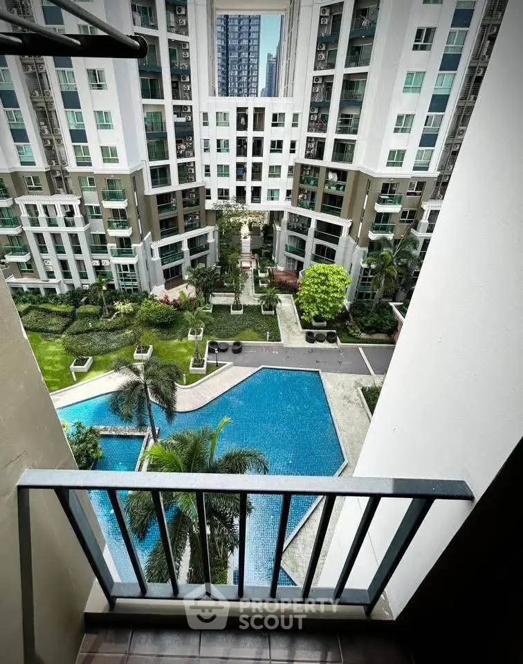 Stunning view from balcony overlooking modern apartment complex with pool and lush garden.