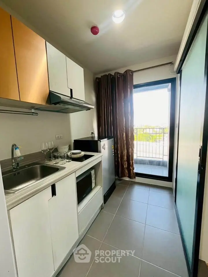 Modern kitchen with sleek cabinetry and balcony view, featuring a compact design and ample natural light.