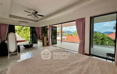 Luxurious bedroom with expansive balcony and stunning view of lush greenery and rooftops.
