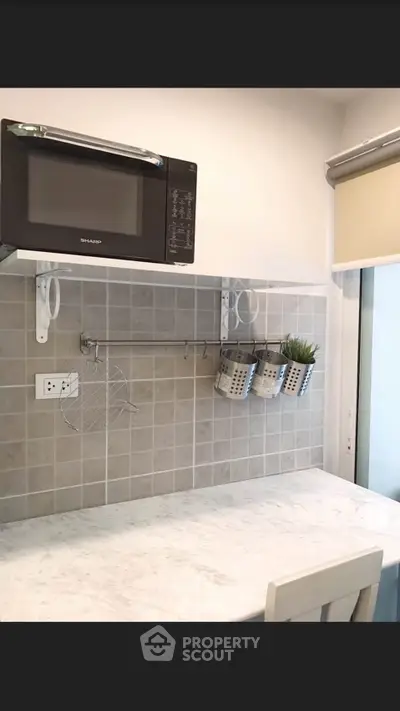 Modern kitchen with microwave and stylish backsplash, featuring a sleek countertop and hanging storage.