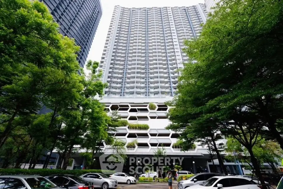 Modern high-rise building with unique facade and lush greenery in urban setting.