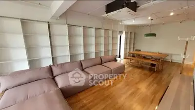 Spacious modern living room with large sofa and dining table, featuring wooden flooring and open shelving.