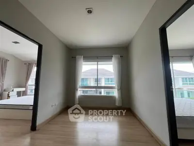 Spacious bedroom with large window and wooden flooring, offering a bright and airy atmosphere.