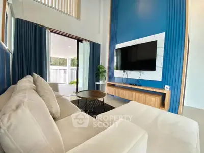 Modern living room with stylish blue accent wall and large TV, featuring cozy beige sofa and open patio view.