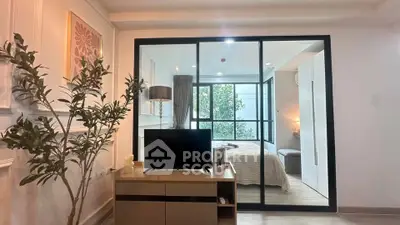 Modern living room with glass partition to bedroom, stylish decor and natural light.