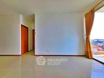Spacious empty room with large window offering city view and natural light.