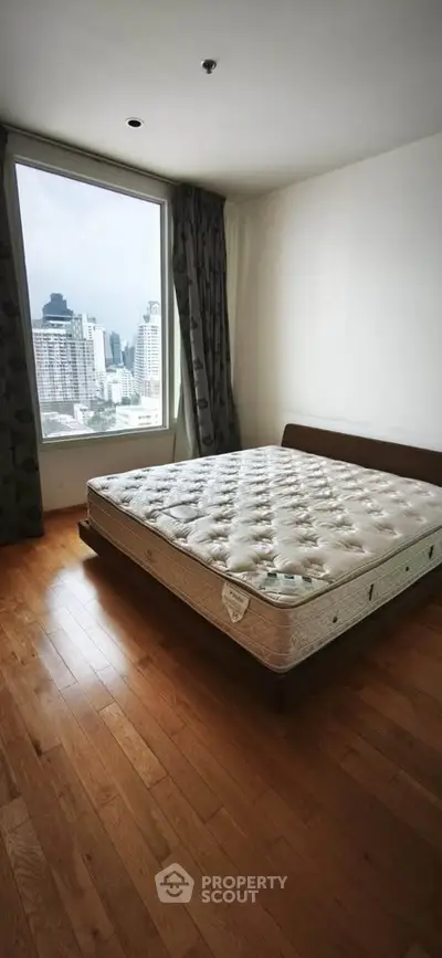 Spacious bedroom with city view and hardwood floors in modern apartment.