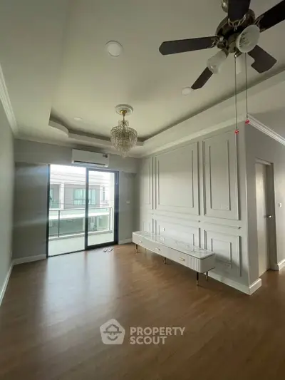 Elegant living room with chandelier and ceiling fan, featuring large windows and stylish wall paneling.
