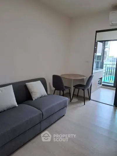 Modern living room with gray sofa and dining area, featuring a balcony view.