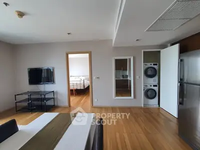 Modern apartment interior with open living area, visible bedroom, and in-unit laundry appliances.