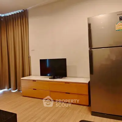 Modern apartment interior with sleek fridge and TV on wooden cabinet, perfect for urban living.