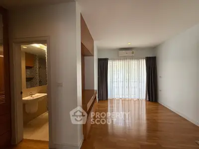 Spacious living room with wooden flooring and natural light, adjacent to a modern bathroom.