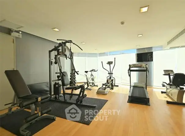 Modern gym with state-of-the-art fitness equipment and natural lighting in luxury apartment building.