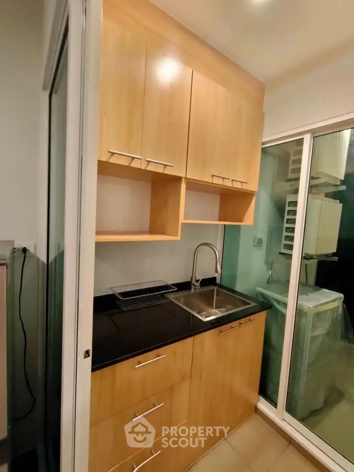 Compact kitchen with wooden cabinets and sliding glass door, featuring a sleek sink and modern design.