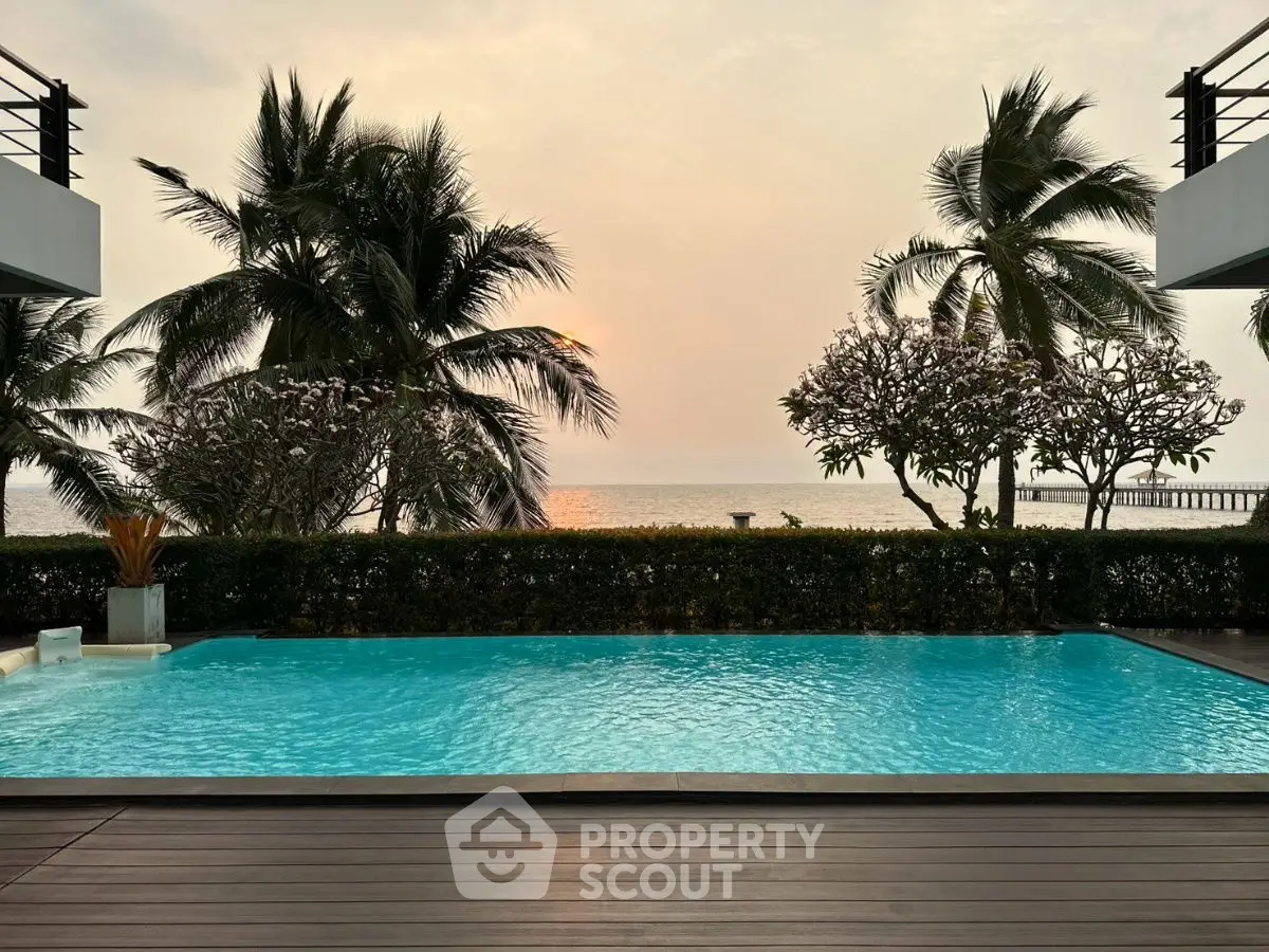 Luxurious beachfront pool with stunning ocean view and palm trees at sunset.