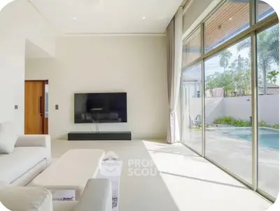 Spacious living room with large windows overlooking a pool, featuring modern decor and ample natural light.