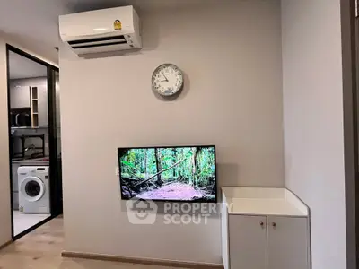 Modern living room with wall-mounted TV and air conditioning unit, featuring a washing machine in the background.