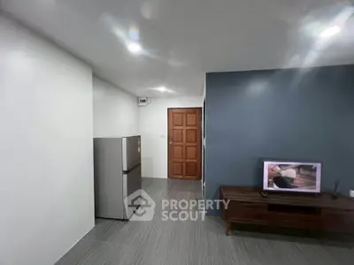 Modern living room with sleek design, featuring a TV and stainless steel fridge, perfect for urban living.