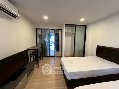 Modern bedroom with twin beds, sleek furniture, and glass sliding doors leading to a bright living area.