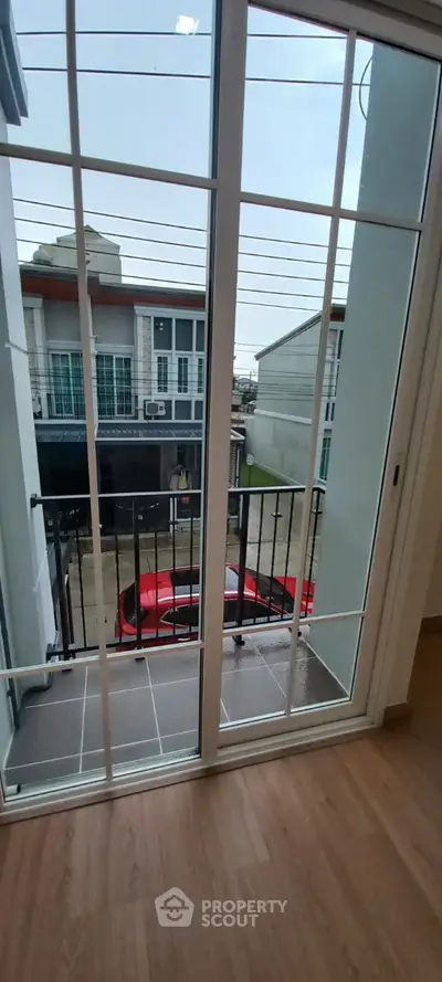 Modern balcony view with sliding glass doors overlooking residential street and parked red car.