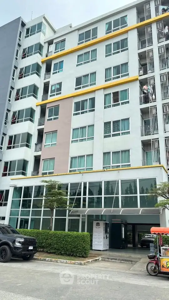 Modern multi-story apartment building with glass entrance and parking area, ideal for urban living.