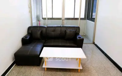Modern living room with sleek black sofa and white coffee table in bright space.