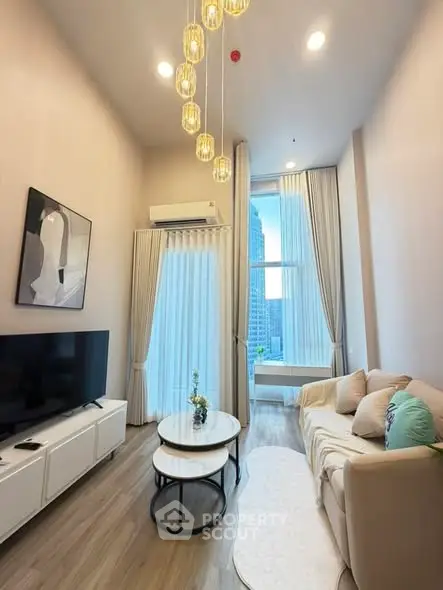 Modern living room with high ceilings, elegant chandelier, and city view through large windows.