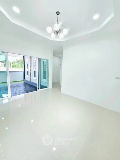 Spacious modern living room with elegant chandelier and large windows opening to a patio.