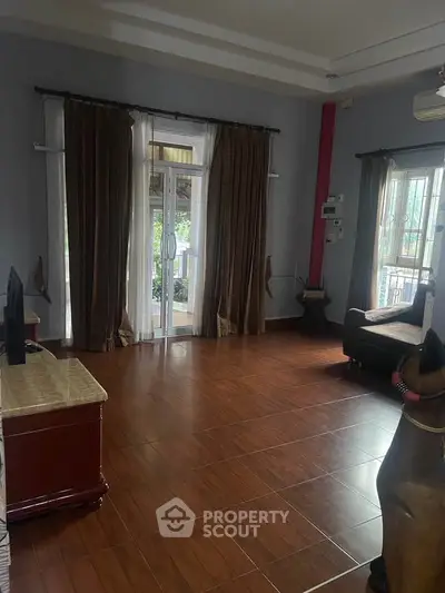 Spacious living room with wooden flooring and large windows opening to a balcony, perfect for natural light.