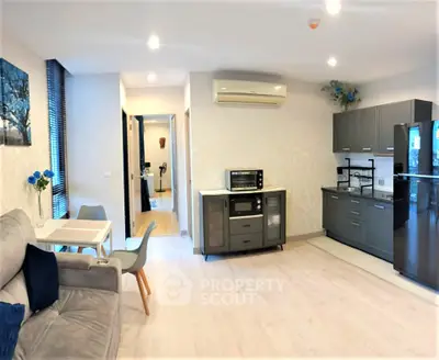 Modern open-plan living room with sleek kitchen and dining area, featuring stylish furniture and bright lighting.