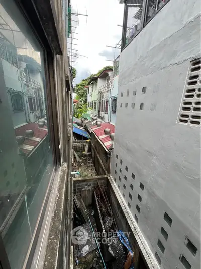 Narrow urban alleyway between residential buildings with a view of rooftops and windows.