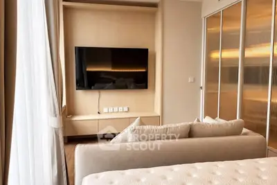 Modern bedroom with sleek TV setup and cozy beige sofa, featuring elegant sliding closet doors.