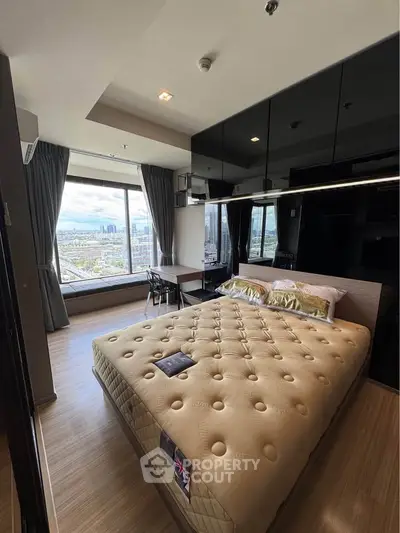 Modern bedroom with large window offering stunning city views, featuring a comfortable bed and sleek furnishings.