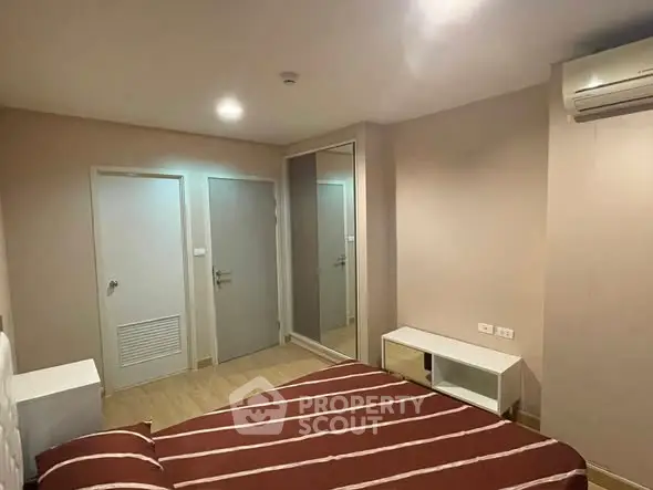 Modern bedroom with striped bedding, mirrored closet, and air conditioning in a cozy apartment.