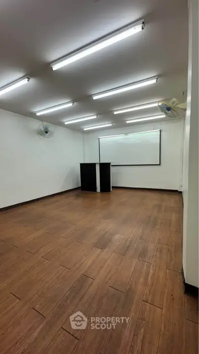 Spacious study room with wooden flooring and ample lighting, ideal for meetings or classes.