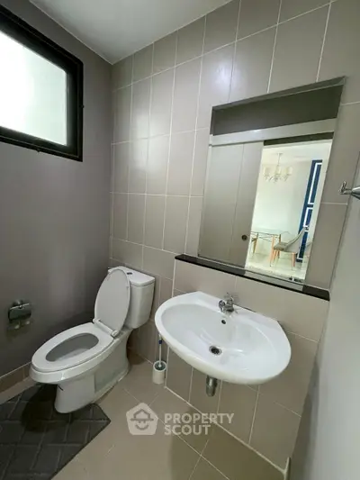 Modern bathroom with sleek fixtures and neutral tiles, featuring a toilet and sink.
