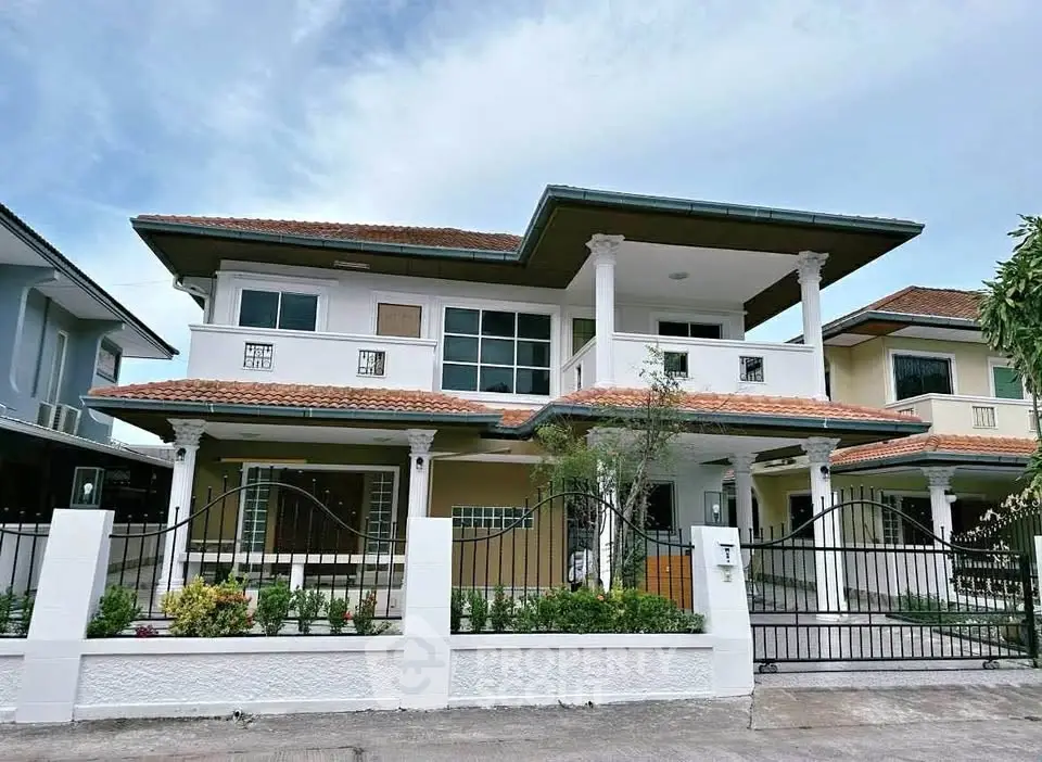 Elegant two-story house with a tiled roof and gated entrance in a suburban neighborhood.