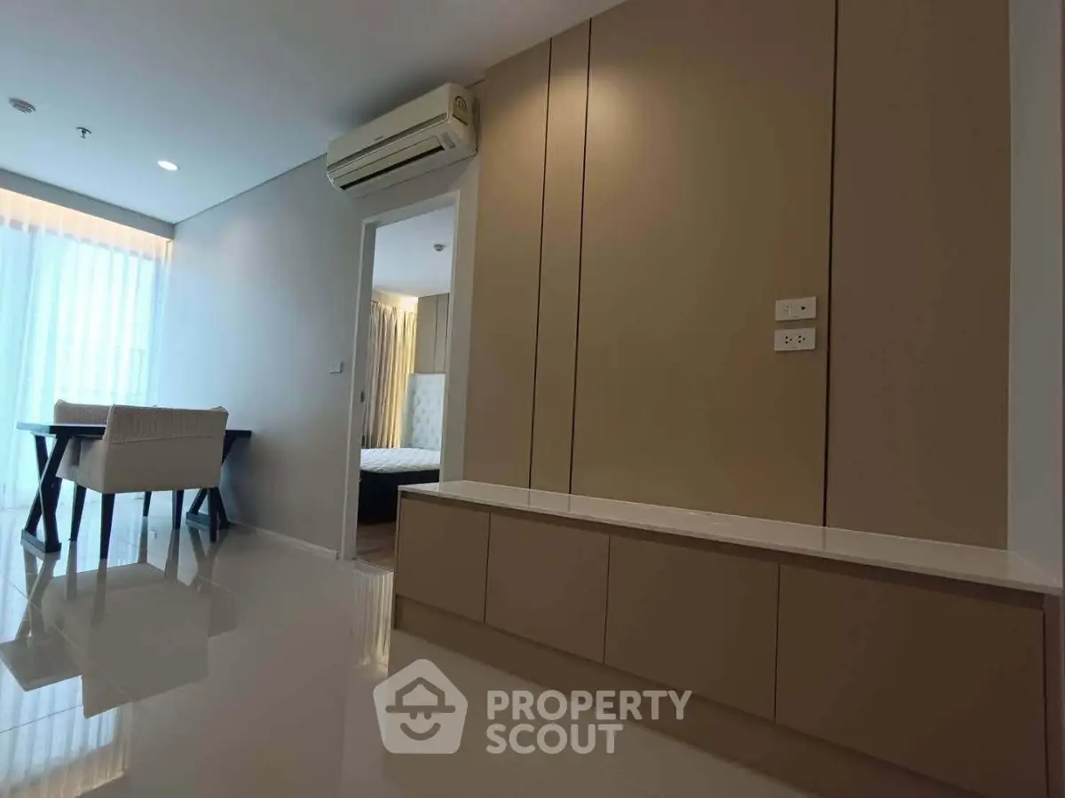 Modern apartment interior with sleek design and natural light, featuring a dining area and bedroom entrance.