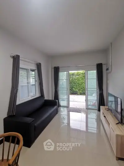 Modern living room with sleek black sofa, large windows, and garden view, perfect for relaxation.