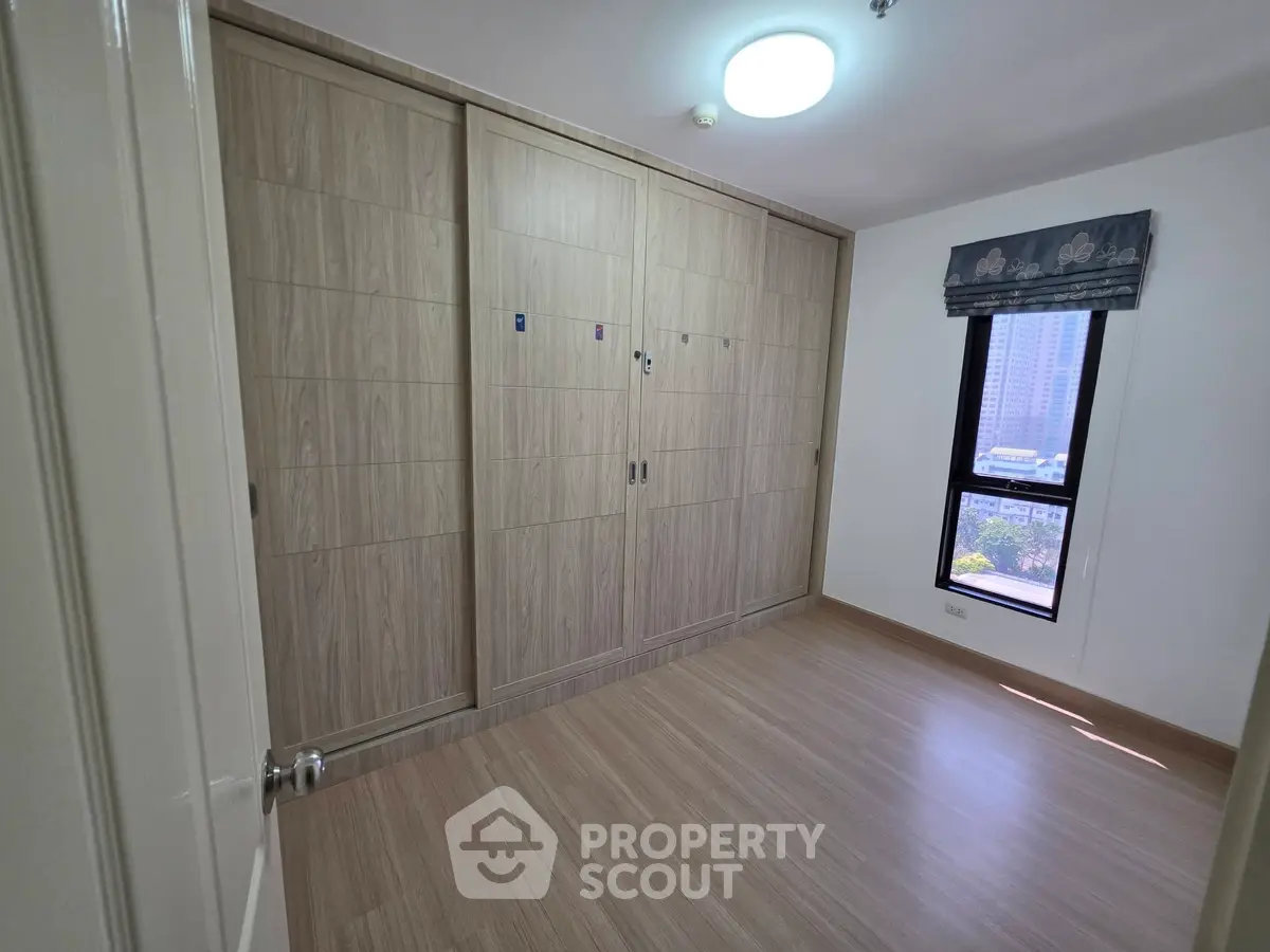 Spacious bedroom with built-in wooden wardrobe and city view window, perfect for modern living.