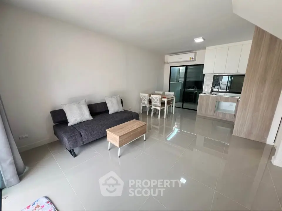 Modern open-plan living room with sleek kitchen and dining area, featuring stylish furniture and glossy tiled floors.