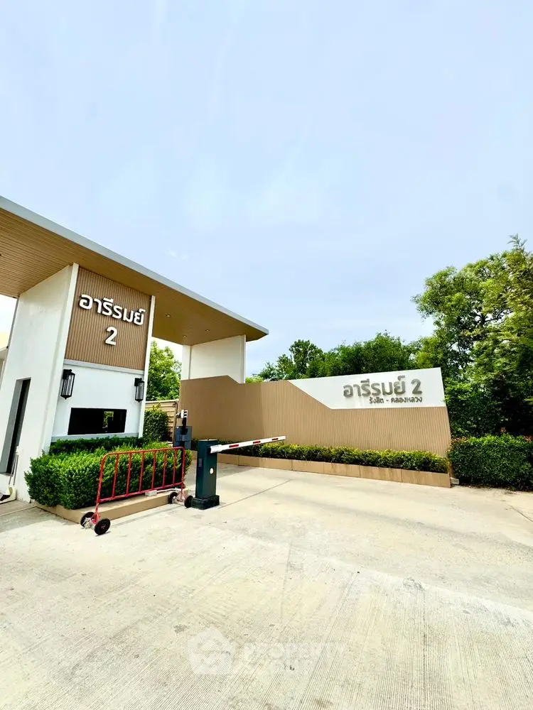 Modern entrance to residential complex with lush greenery and secure access.