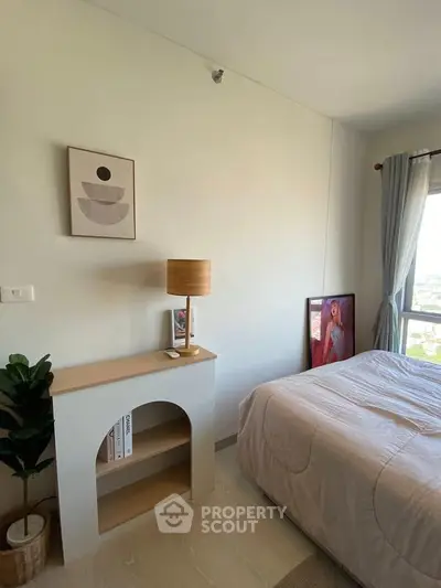 Cozy bedroom with modern decor and natural light, featuring a stylish lamp and artwork.