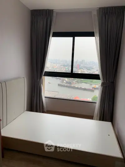 Cozy bedroom with stunning city and river view from large window, perfect for urban living.