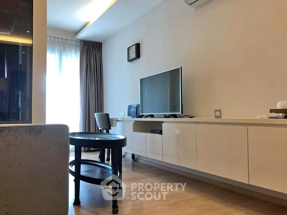 Modern living room with sleek furniture and large TV, featuring natural light and elegant decor.