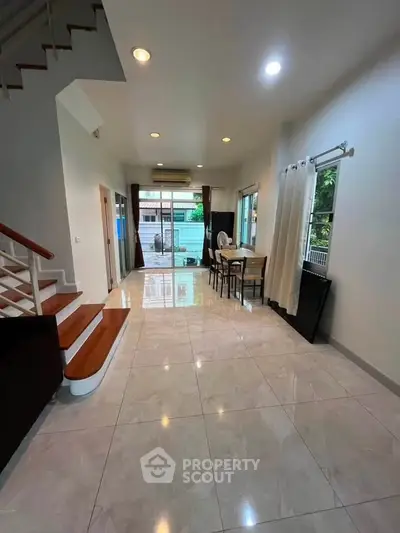 Spacious modern living room with dining area and staircase, featuring large windows and elegant tile flooring.