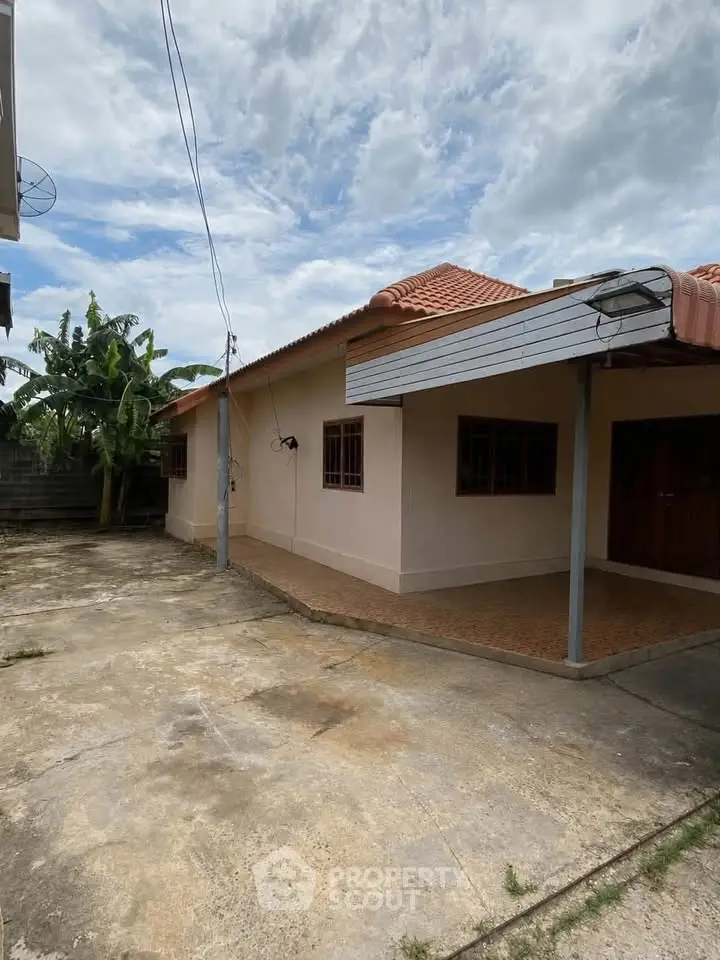 Charming single-story home with spacious driveway and lush banana trees in the backyard.