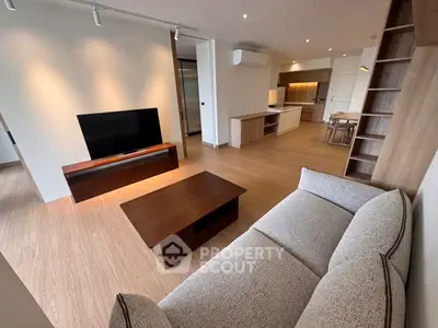 Spacious modern living room with open kitchen, cozy sofa, and sleek wooden furniture.