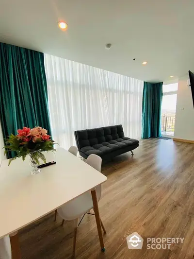 Modern living room with large windows, stylish sofa, and elegant dining area, featuring wood flooring and teal curtains.